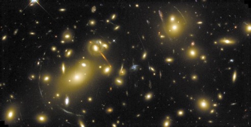 図3　ハッブル宇宙望遠鏡で撮られた遠方の銀河団 Abell 2218。多数の銀河が密集して宇宙のメガロポリスを形成している。同心円状に広がるアークは，銀河団背後にあるより遠方の銀河の光が重力レンズ効果により結像したもので，アインシュタインの一般相対性理論から予言されていたもの。
